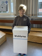 Ein Schüler welcher eine Wahlurne bei den Juniorwahlen Kids hält.